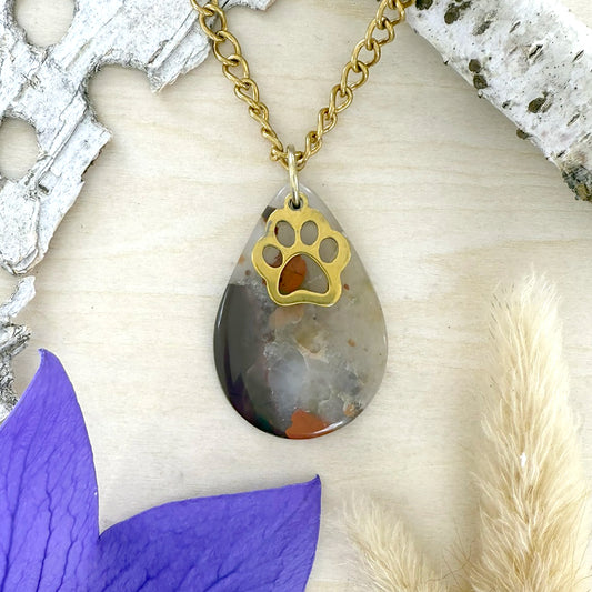Necklace with a teardrop pendant featuring a paw print design, set against a natural wood background.