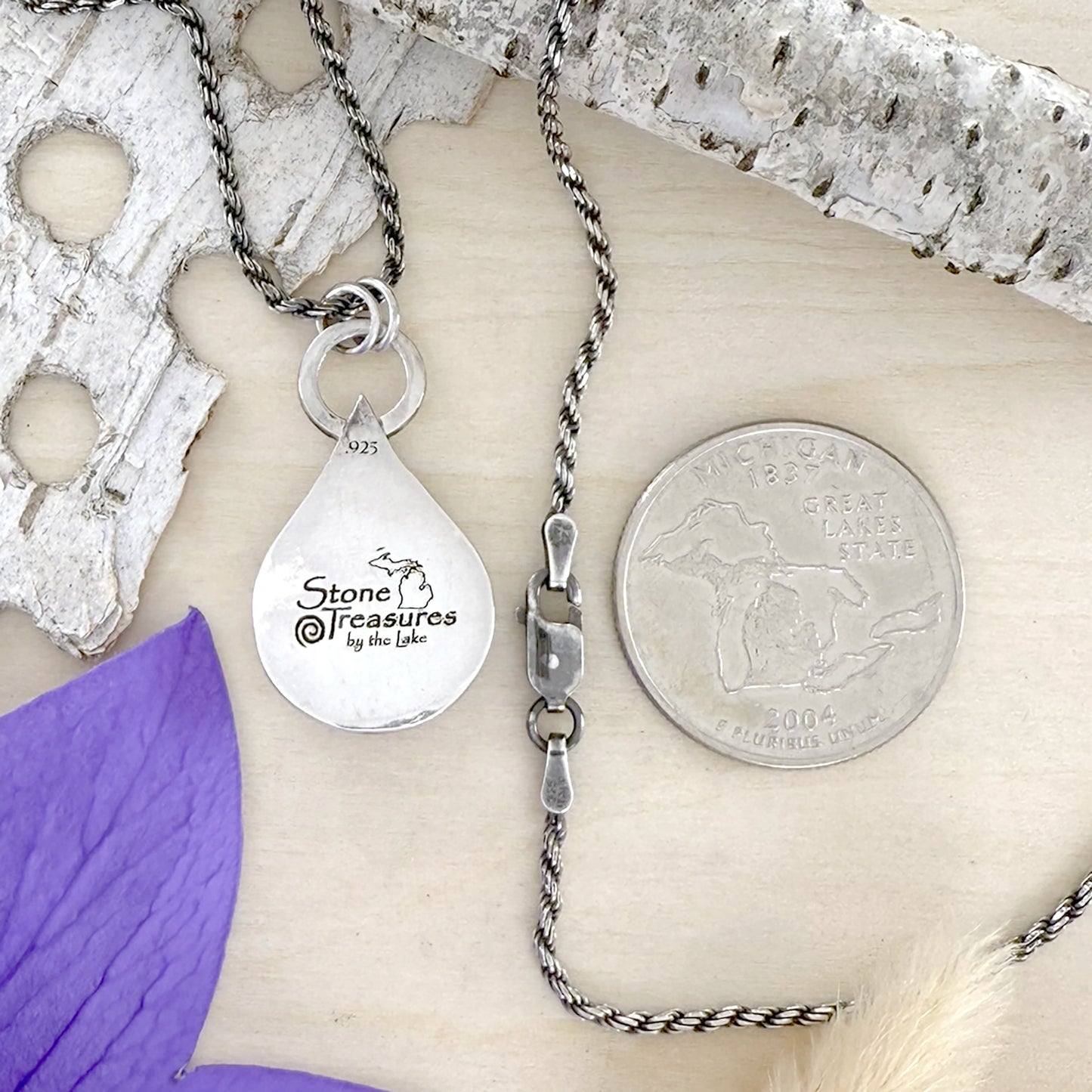Silver necklace with a teardrop pendant on a wood background, featuring 'Stone Treasures by the Lake' branding.