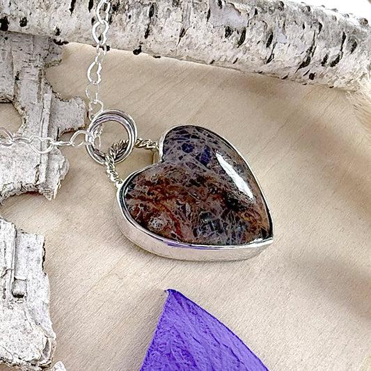 Heart-shaped pendant with a textured surface on a chain, set against a natural wood background.