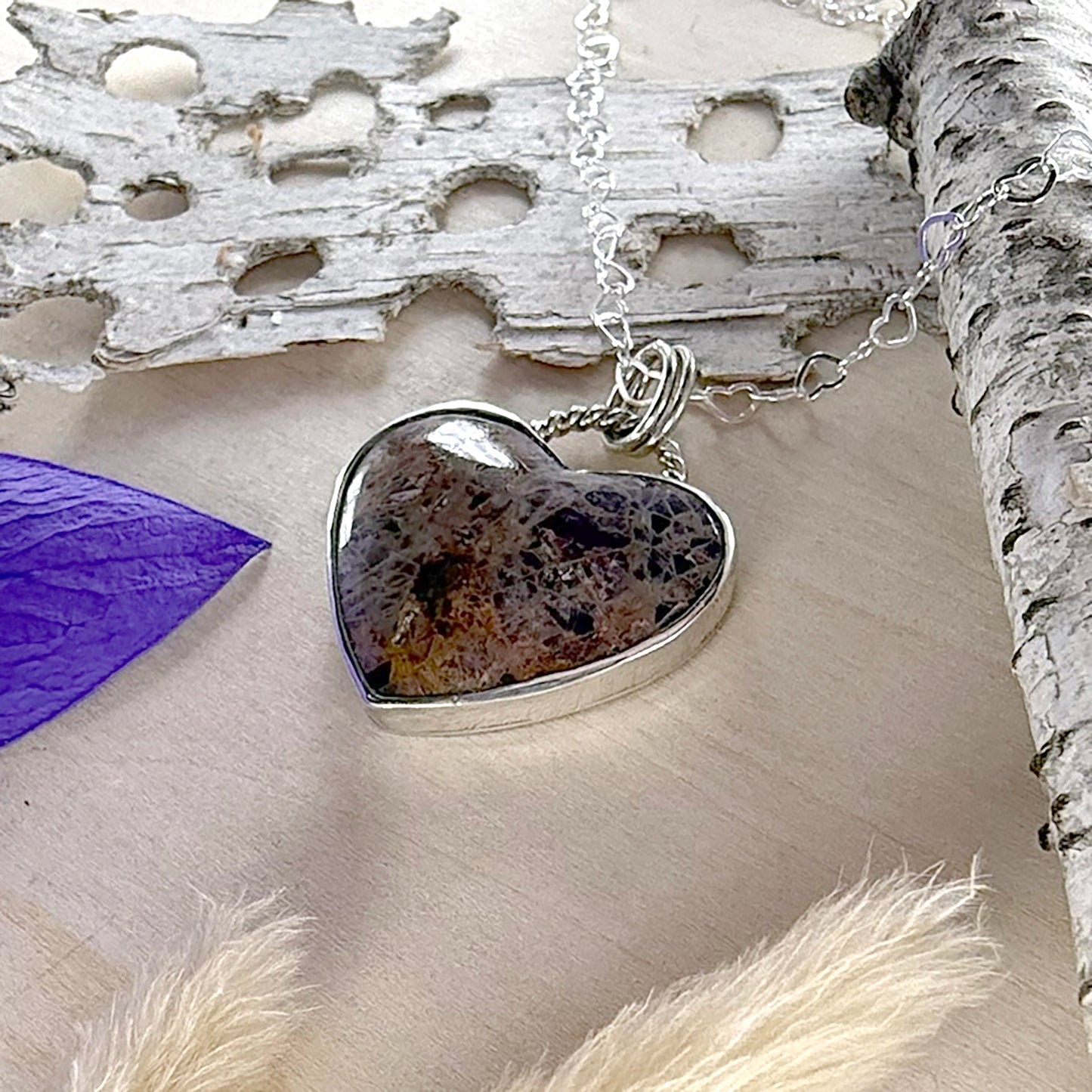 Heart-shaped stone pendant on a silver chain against a natural background with wood.