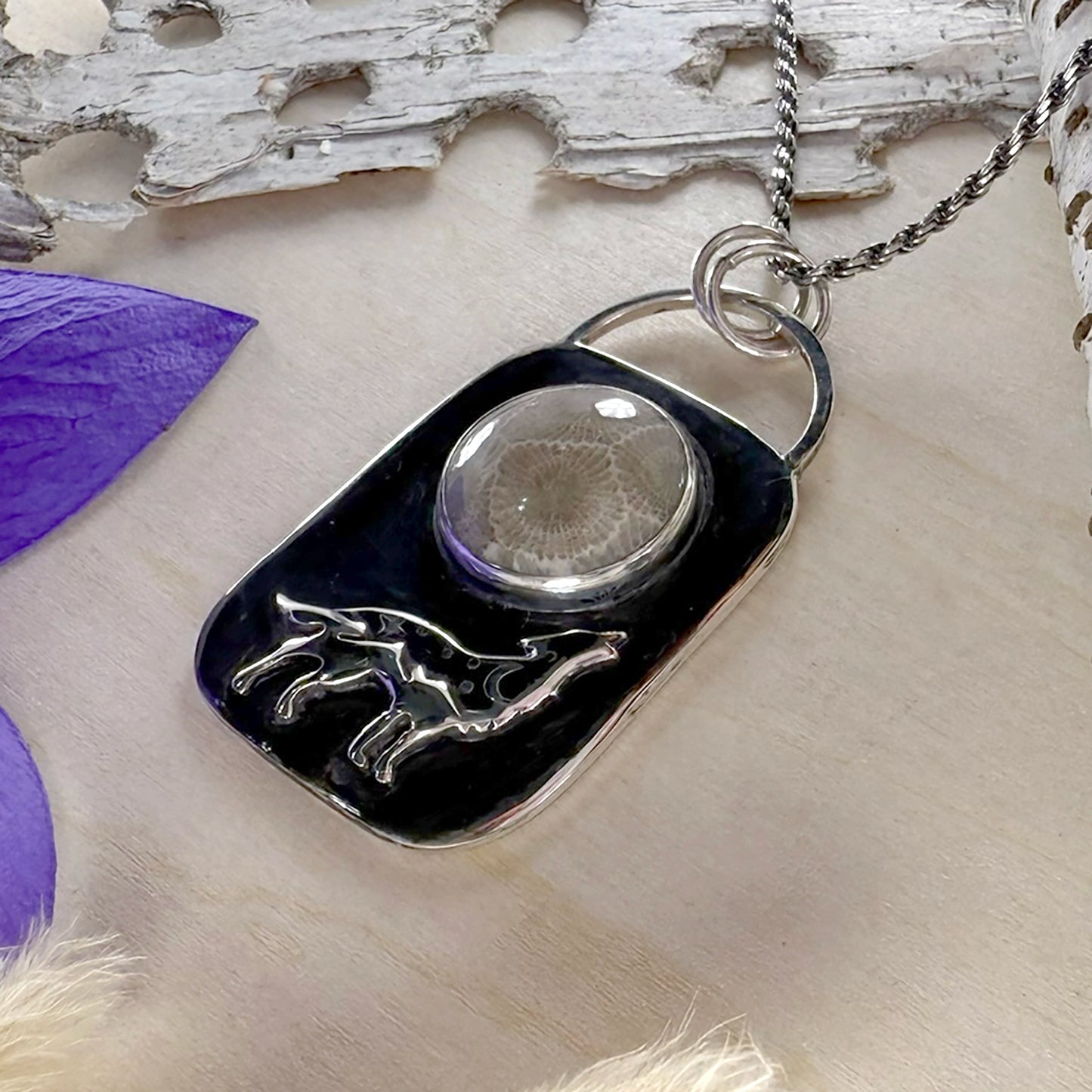 Silver pendant with black background and animal design on a wooden surface