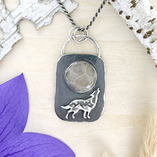 Silver pendant with wolf design on a wood background