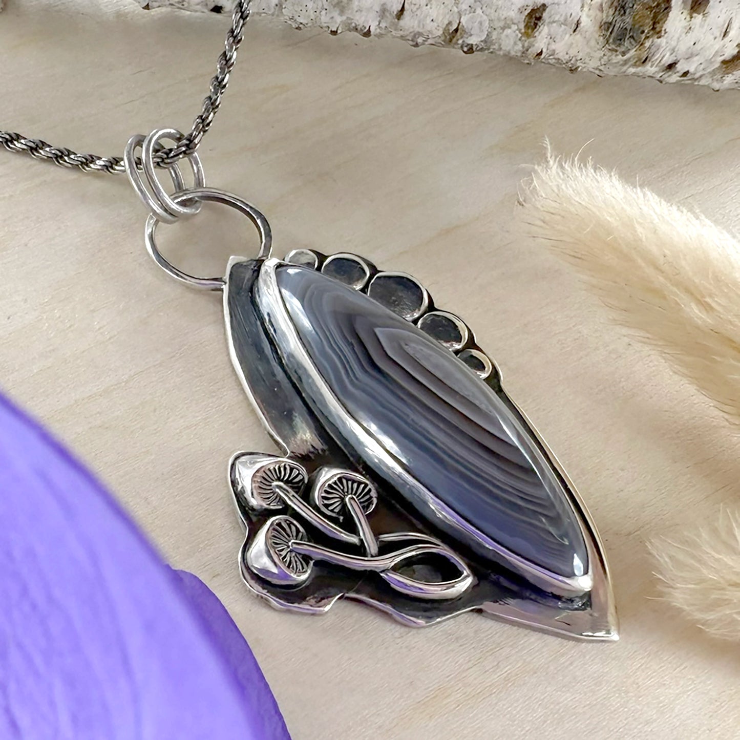 Silver pendant with a purple stone on a neutral background