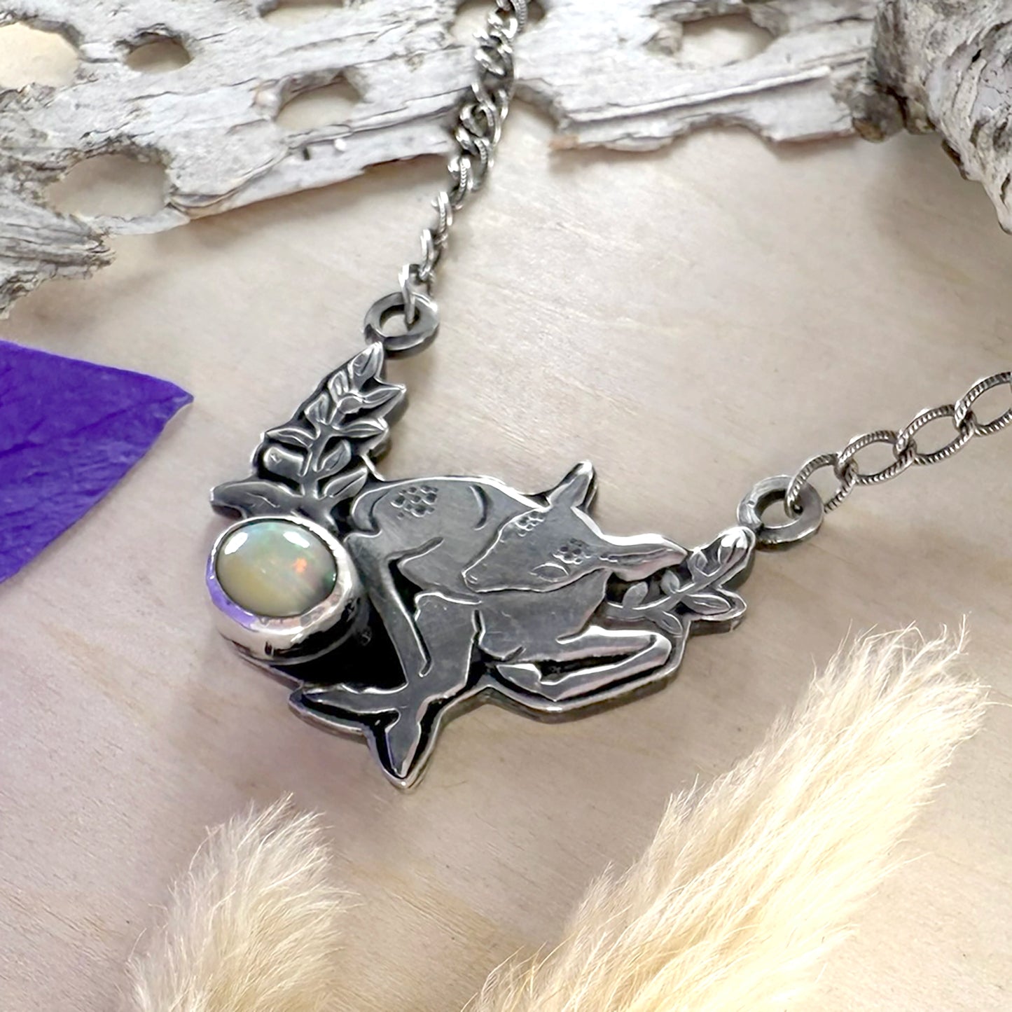 Silver necklace with a pendant featuring a deer and opal on a natural background.