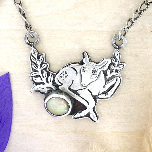 Silver fawn pendant with an opal on a chain against a beige background