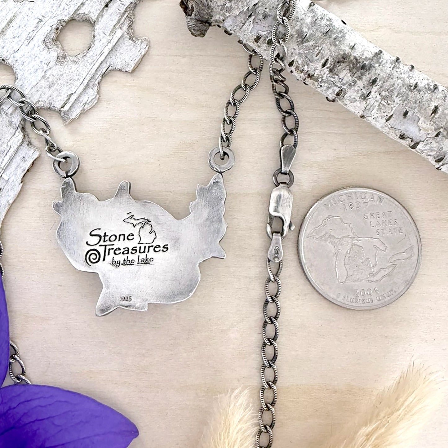 Silver Pendant with a 'Stone Treasures by the Lake' charm on a wooden surface.