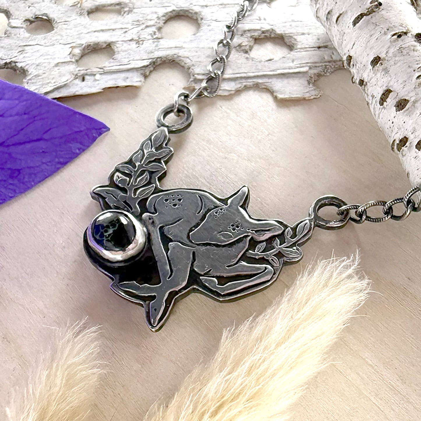 Silver necklace with a deer pendant on a wood surface