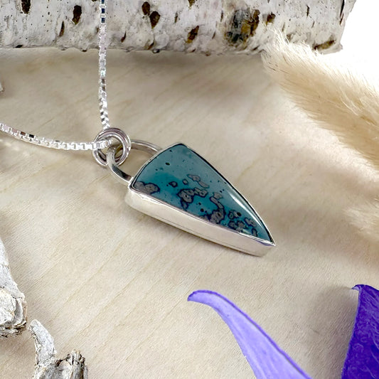 Silver necklace with a blue pendant on a textured surface