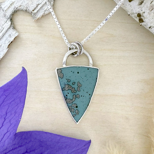 Necklace with a triangular Leland Blue  pendant on a textured surface