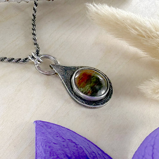 Silver teardrop pendant with floral design on a wood background