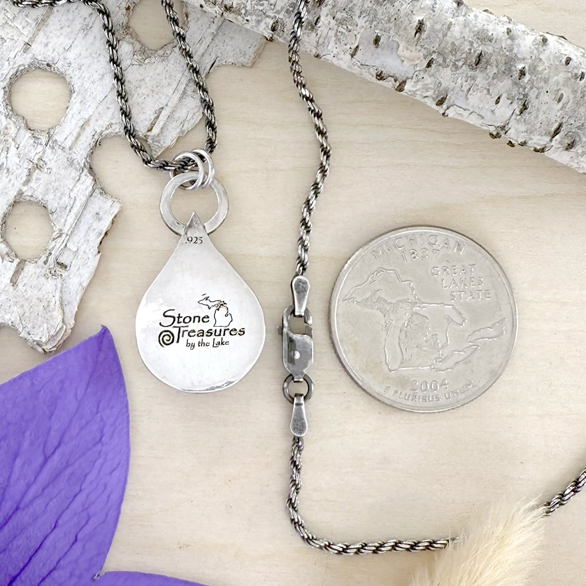 Silver necklace with a teardrop pendant on a wood background, featuring 'Stone Treasures by the Lake' branding.