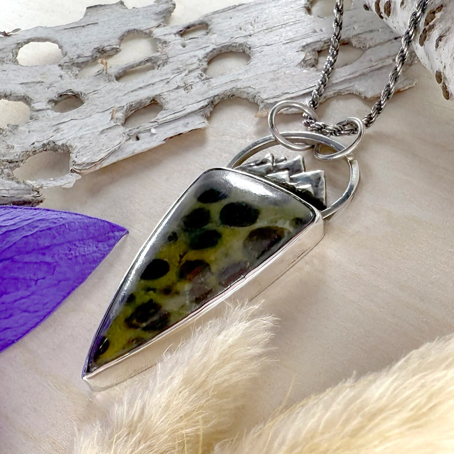 Silver pendant with a speckled stone on a natural background