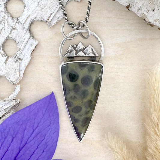 Necklace with a pendant featuring a mountain design on a textured surface