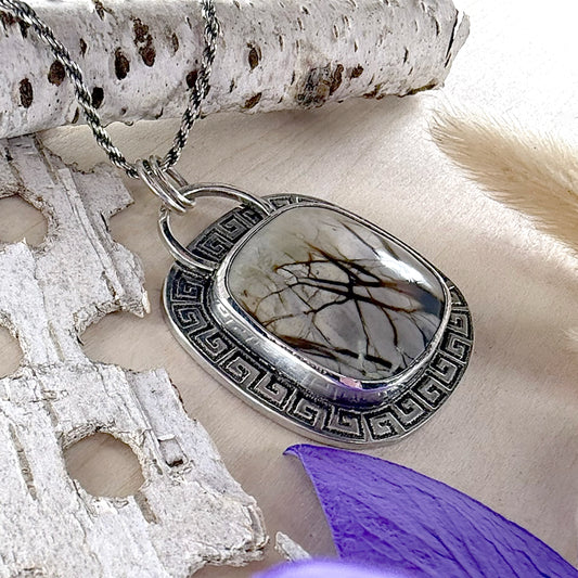Silver pendant with a stone-like center on a wood surface with natural elements.