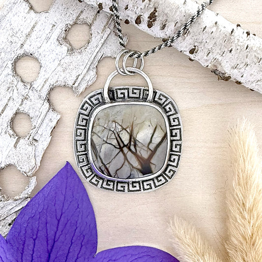 Silver pendant with tree design on a textured surface