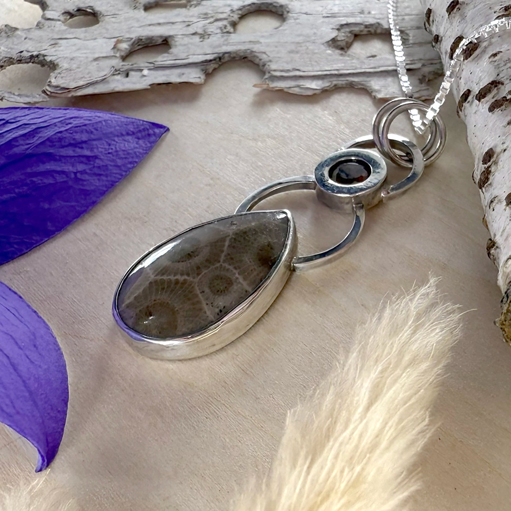 Silver pendant necklace on a natural background with purple petals.