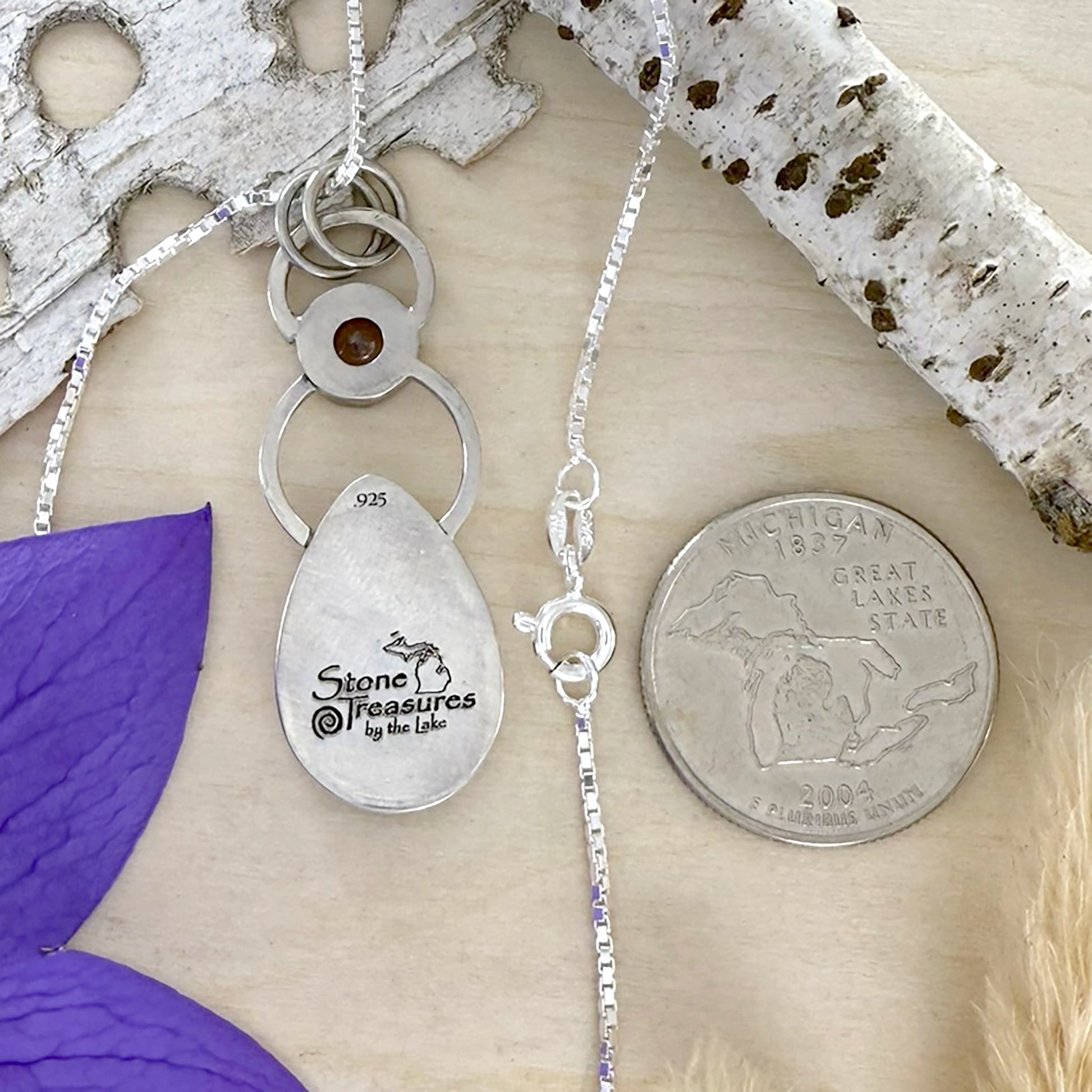 Silver necklace with a pendant on a wooden surface next to a coin for scale.