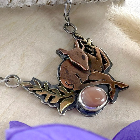 Metallic pendant with a design of a deer and leaves on a textured surface.