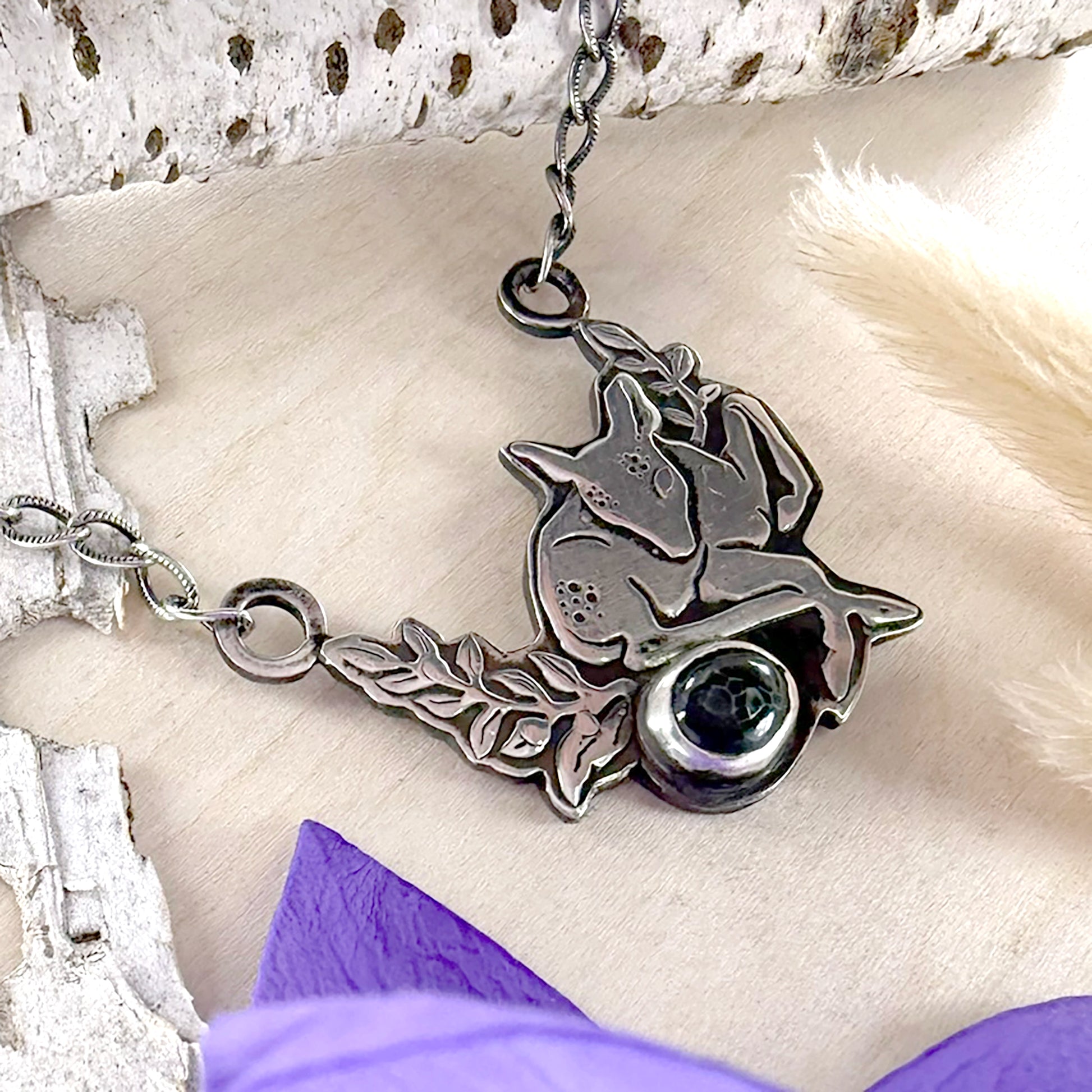 Silver necklace with a pendant featuring a deer and a stone on a textured surface.