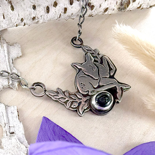 Silver necklace with a pendant featuring a deer and a stone on a textured surface.